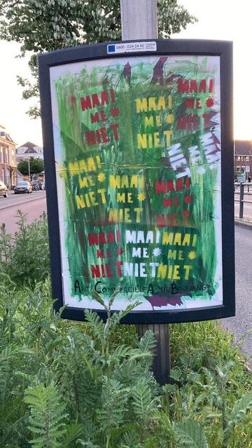 reclame bord in berm  met gras en plantjes met groene kleuren alsof het gras is, met in rood, geel en wit 10x 'maai me niet *' gesprayed