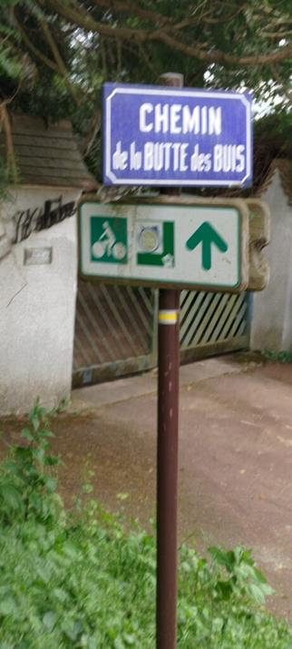 Photo floue d'un panneau de rue "Chemin de la Butte des Buis" et un panneau de voie cyclable "La Véloscénie"