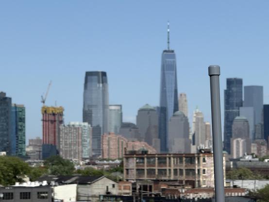 Grey stick of an antenna sticks up in front of the downtown Jersey city and lower Manhattan skyline.