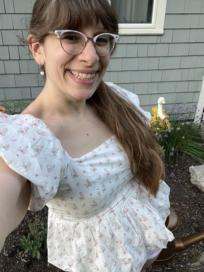 A picture of Blankit smiling brightly in front of a flower bed