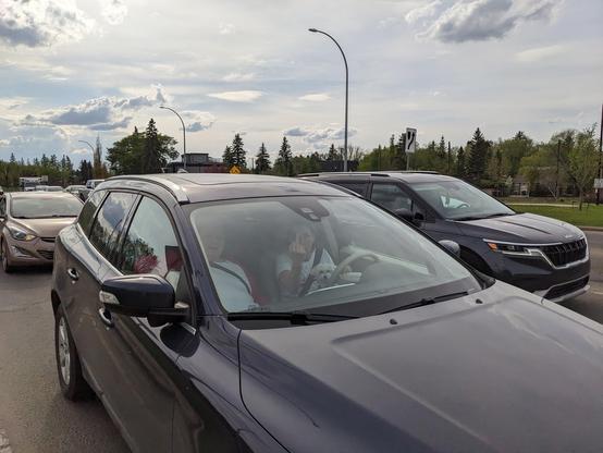 Driver with dog on lap throwing a middle finger; feelings of the older lady beside her, likely her mother, unknown.