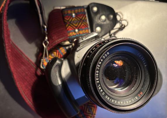 20-year-old 35mm Canon camera with burgundy, patterned, camera strap. It is sporting an 80mm Zeiss lens with red “MC” meaning multi-coated lens.