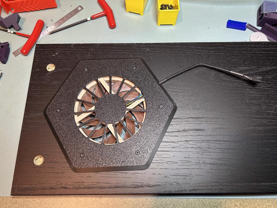 The bottom side of the shelf shows the bottom side of the hexagonal surround installed with the fan inside.  Six socket head screws hold it together, and the cord is routed toward the center of the shelf.