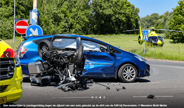A blue car, with a dented side. A motorcycle lays in front of it, it's upside down. A nose of an ambulance is visible in the left side of the picture. Text on the picture says that a motor driver has crashed into the side of a car on the exit of the A58 (which is wrong, it was the A50). And it states the copyright by Meesters Multi Media.