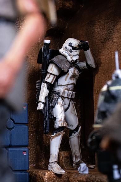 A sandtrooper from Star Wars leans against a brown wall in an exhausted posture. He is filthy. He is also a toy.