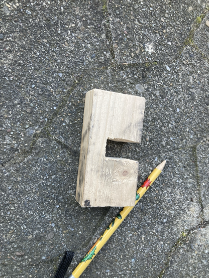 Ein Stück Dachlatte etwa so lang wie ein Bleistift. In U-Form wurde etwas ausgesägt, damit von unten der Rahmen an die Platte geklemmt werden kann.