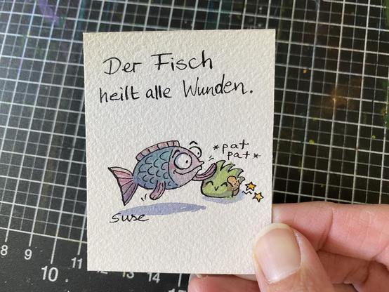 "Der Fisch heilt alle Wunden." Ein Fisch der ein Strüppi tätschelt, das ein Pflaster hat.