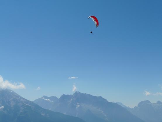 Rotweißer Paraglider am Himmel über den Bergen rund um den Königssee
Der Himmel ist strahlend blau mit nur wenigen Wölkchen