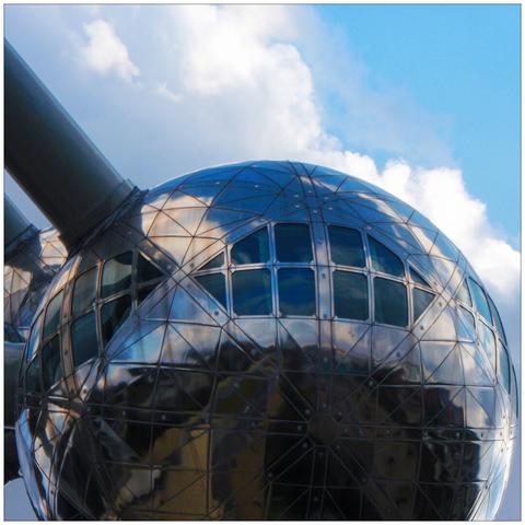 Close-up of one of the aluminum spheres of the Atomium with panorama windows and connecting steel tubes to the left against a blue sky with white clouds.