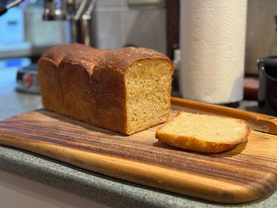 A three domed sandwich loaf, with one slice cut from the end. The crumb (inside) is a golden brown.
