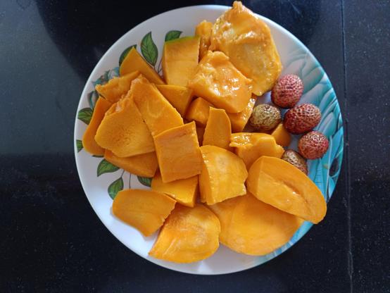 A plate that has 5 litchis and many ripe mango pieces.