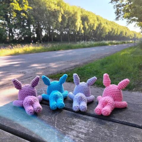 A picture of four crocheted bunnies lying down on their bellies, facing away from the camera, on a picnic table, next to a canal.