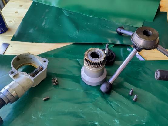 The quill feed mechanism disassembled for cleaning. Shown to the right is the course quill feed with the three handles and the first part of the conical clutch. This handle dirrectly drives quill axle dirrectly via an key drive. In the middle is the worm-gear sproket that is driven by the worm gear and moves freely over the quill axle. This sproket has the second part of the conical clutch. To the left is the fine quil feed housing with wormgearing. This drives the sproket and holds it in place.

The way the fine quill feed works: The course quill feed (on the right) drives the quill. With an hand screw you force the course quill feed handle into the sproket of the worm-gear. This enables to clutch with friction. Now you can drive the quill with the fine adjustment. To drive the quill with the course adjustment you need to unscrew the clutch. This way the sproket rotates freely over the quill axle/shaft and the course wheel is no longer linked to the fine feed mechanism.