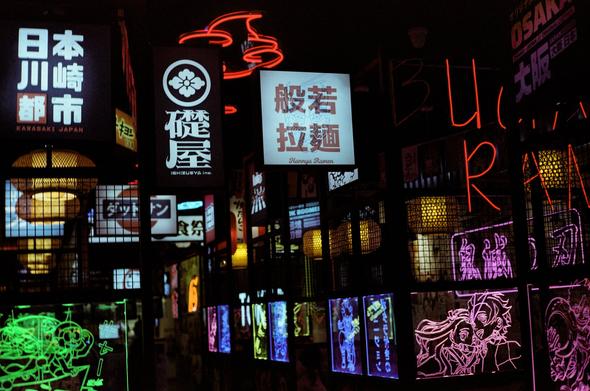 Night color photography of a ramen place full of neon lights. There are Japanese ideograms and manga illustrations.