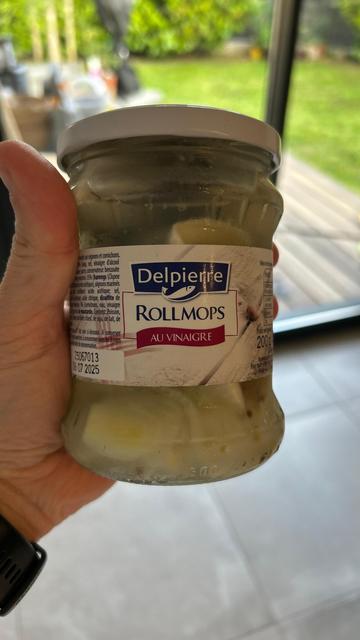 Mão de homem branco segurando um pote de vidro fechado, com uma conserva de Rollmops.