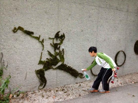 Youth spraying water on a moss graffiti of a human figure in a martial arts exercise pose.