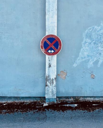 Ein leicht verschlissenes Schild für absolutes Halteverbot hängt an einer bläulichen verschlissenen Wand.