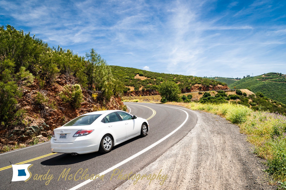 Car driving through an “S” curve in the foothills under a blue sky.