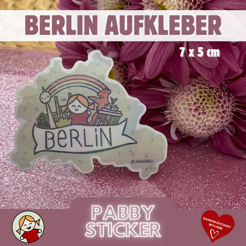 Handgemachter Berlin-Sticker mit Fernsehturm, Olympiastadion, Brandenburger Tor, Berliner Bär, Regenbogen und meiner Signatur-Figur Pabby. Die Grundform ist die Silhouette der Stadt Berlin. Im Hintergrund zartlilafarbene Blumen.