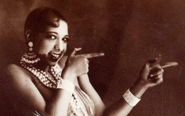 Josephine Baker with short wavy hair, scantily clad, but covered in jewelry, smiling and pointing with the index fingers of both of her hands as though she were meaning to say "check this out!"
(It's a cropped image from the Banana Skirt publicity photo (from the Folies Bergère production "Un Vent de Folie").)