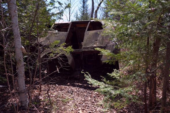 A rusty large vehicle, turned almost to the side so that you can see the underside. Dense bush all around it.
