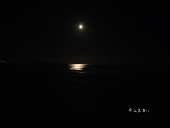 Nuit noire. Une minuscule pleine lune se reflète sur l'eau calme de la mer.