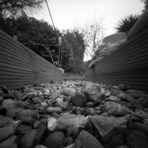 Camera at ground level looking down a gravel path between two raised vegetable beds