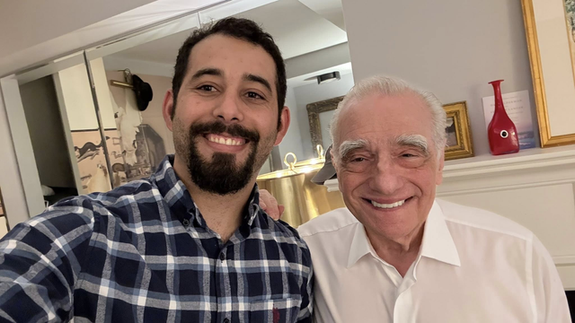Photo of Mosab Abu Toha and Martin Scorsese in a living room setting, standing side by side smiling into the camera. Martin has his right hand on Mosab’s left shoulder.