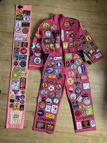 A pink boiler suit and a long pink scarf covered in embroidered patches. The scarf has been folded in half.