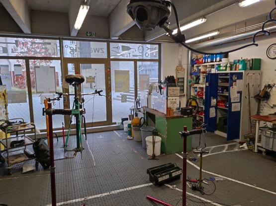 Eine Fahrradwerkstatt mit allerhand technischem Gedöns, mittendrin ein Fahrrad auf einem Montage-Ständer.