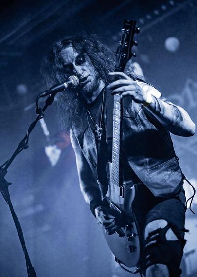 Sänger der Black/Death/Doom Band "Horns Of Domination" mit der Gitarre in der Hand vor dem Mikro.
