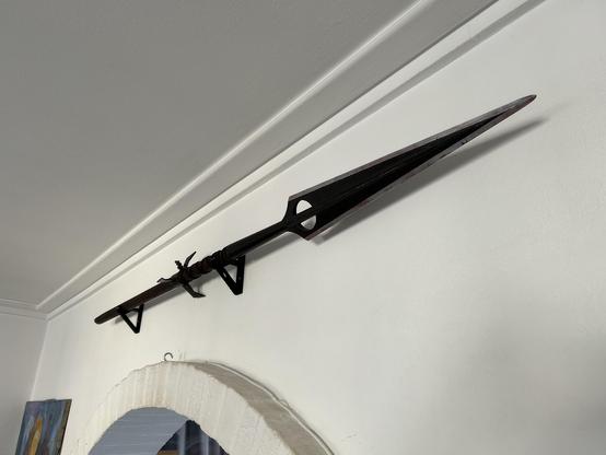 Dragonslayer spear prop replica mounted on the wall, resting horizontally in a pair of cradle brackets