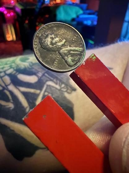 A silver colored but extremely dirty US penny dating from 1945. It stands balanced on one edge unaided at the end of a red U magnet.