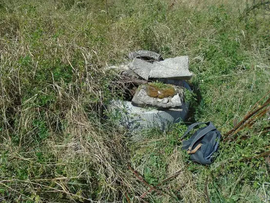 The image shows a pile of broken concrete pieces resting in a grassy area. There appears to be some vegetation surrounding the concrete, and a bag or piece of fabric is partially visible in the lower right corner. The overall scene has an unkempt and natural look, indicating it might be an abandoned or overlooked site.

Image Credits: Wikimedia / Szenti Tamás / CC BY-SA 4.0