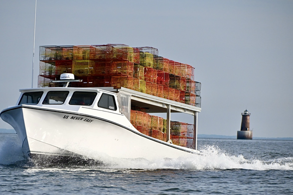 Crab boat  on plane, piled high with colorful crab pots. The Bloody Point lighthouse in the background