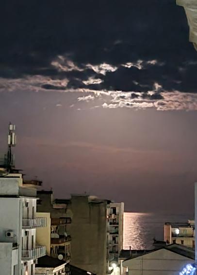 Nuvole coprono la luna che tuttavia illumina uno specchio di mare tra i palazzi di città
