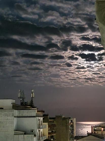 Nuvole coprono la luna che tuttavia illumina uno specchio di mare tra i palazzi di città
