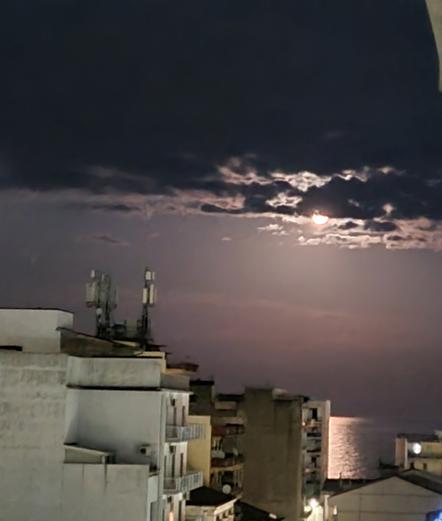 Nuvole coprono la luna che tuttavia illumina uno specchio di mare tra i palazzi di città