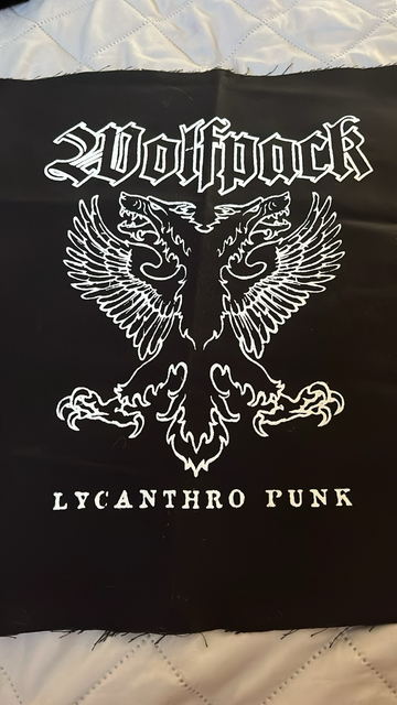 A black back patch with the wolf pack band name on top in white on. The band’s wolf eagle mascot is in the middle in white. The words Lycanthro punk are on the bottom in white underneath the mascot.