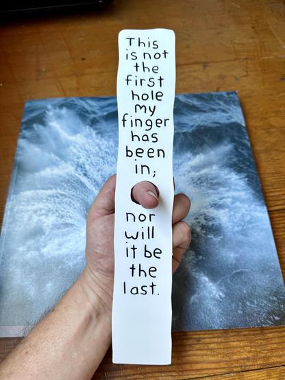 The cover of Issue 2 of Inscription Journal, and a bookmark with a finger hole and finger through it. The bookmark is by Miranda July and has the this written on it "this is not the first hole my finger has been in; nor will it be the last"