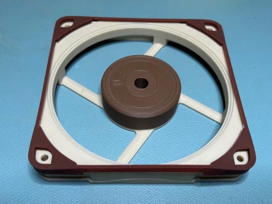 A 3D printed repllca of a Noctua fan.  It has the same colors and shape, but there are no blades.  There is a flexible rubber surround (original Noctua part) around the fan's top perimter.