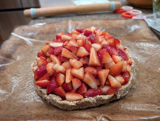 unbaked crostata with extremely short walls, loaded with about 4x the appropriate amount of cut strawberries, sitting on a thin silicon baking sheet in a quarter sheet pan