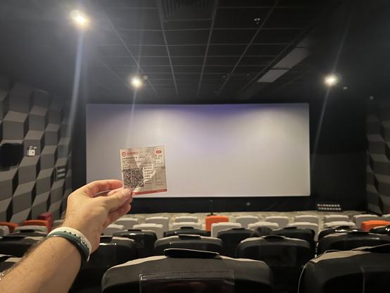 An arm holding out a movie ticket in a mostly empty theater