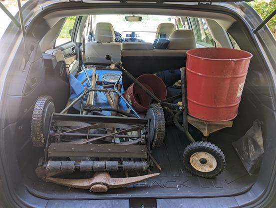 Back of a Subaru Outback filled with yard tools: hand tools plus two seed spreaders and a reel mower. All of that was dropped off at the salvage shed at the recycling center.