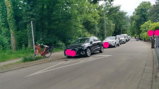 Fahrradstraße mit massenhaft am "Fahrbahnrand" abgestellten KFZ. Ein abgestellter PKW steht auf auf einem Riesen-Piktogramm "Achtung Kinder".