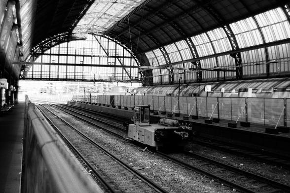 Black & white photo of the tracks and arching roof of Amsterdam Centraal station. The platforms have been fenced, I'm guessing because of construction work.