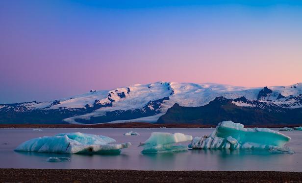 A vividly pink and blue colored sky over Iceland's Jökulsárlón glacial lagoon in mid-summer as thousand year old icebergs slowly make their way to the sea.