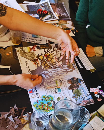 A paper cutout tree being places gently on a collage on a table full of collage materials and scissors.