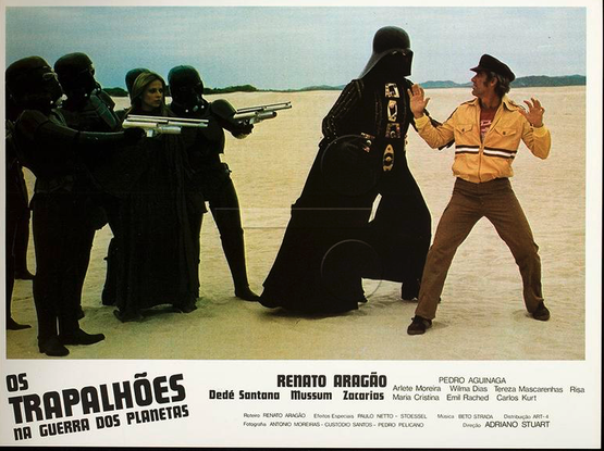 Imagem de impresso de divulgação com cena do filme, na qual o personagem de Renato Aragão ergue os braços em sinal de rendição diante do personagem que parodia Darth Vader, e suas tropas.