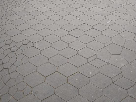 Photograph of grey street paving that consists of symmetrical pentagons in in symmetrical hexagons. The middle has medium-sized hexagons; the left has pentagons inside the hexagons; the right has bigger hexagons with pentagons inside.